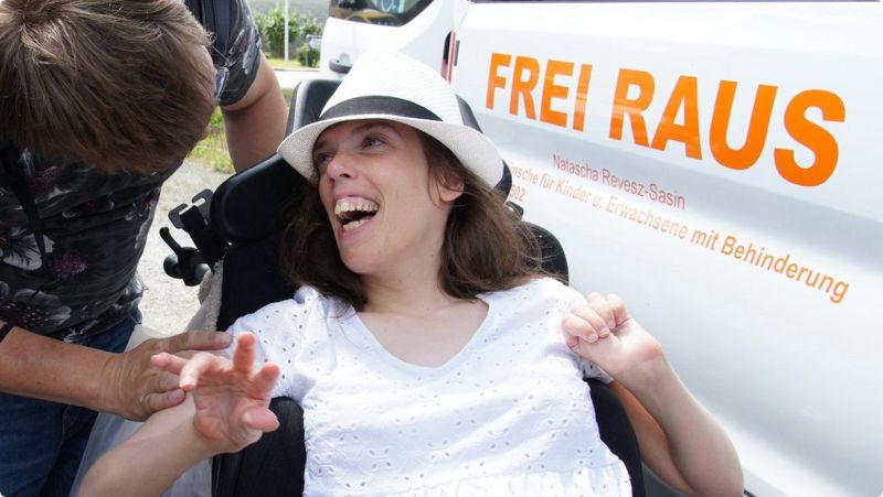 Eine junge Frau mit Sonnenhut lacht vor dem Frei-Raus-Bus.